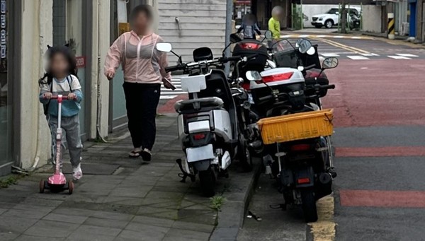 제주지역 스쿨존내 인도 위에 세워진 오토바이 옆으로 한 아이와 부모가 통행하고 있다.